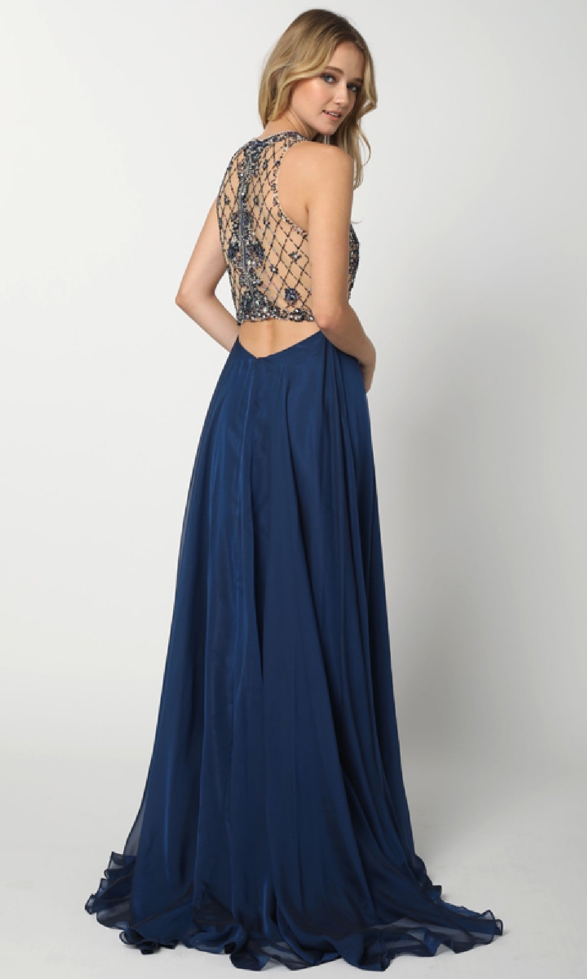 A woman poses with her back to the camera in the Long Prom Dress: Juliet 637, featuring a navy blue sleeveless design, an embellished bodice, a beaded sheer back, and a flowing skirt against a plain background.